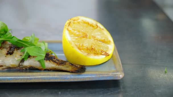 Fish rainbow trout close-up cooked on charcoal grill on plate in restaurant with lemon and arugula greens. video camera slides — Stock Video