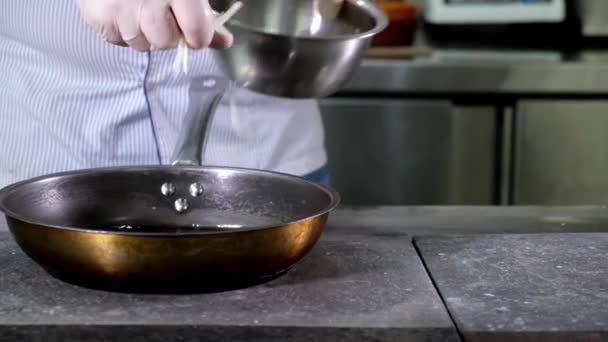 Lokanta mutfağındaki aşçı kendi elleriyle ahşap kaşıkla karıştırarak metal çatal bıçaklardan yapılmış çiğ soğanları kızartma tavasına koyar. Yemek pişirmek için aşçı malzemeleri hazırlıyorum.. — Stok video