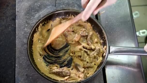 Köksmästare i restaurangkök blandar ingredienser i stekpanna med träskedsvamp, lök, viltkött med grädde och röd sås. Matlagning för besökare. ovanifrån — Stockvideo