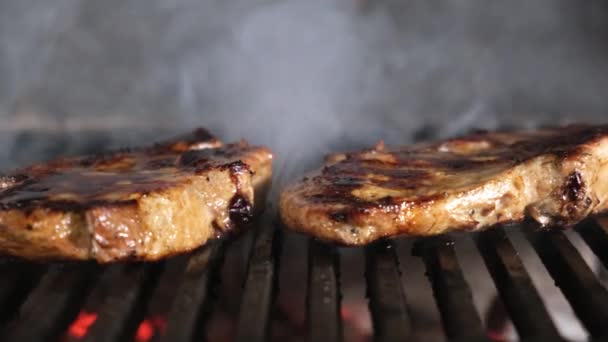 Şef tong 'u kullanıyor ve eti ızgaraya çeviriyor. Ateş yanıyor, sıcak yağlı biftek pişiyor. Izgara, lezzetli biftek yavaş çekimde yakın çekim. — Stok video