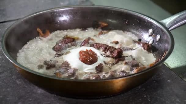 El chef de la cocina del restaurante mezcla ingredientes en la sartén con champiñones de madera, cebollas, carne de venado silvestre con crema y salsa roja. Cocina para los visitantes. plato es frito y hierve en estufa. — Vídeos de Stock