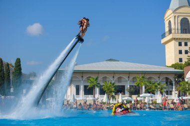ANTALYA TURKEY 27 SEPT 2019: uçuş panosunda genç bir kızla dalış kıyafeti giyen bir adam havuz otelinde uçuyor ya da su basıncı kuvveti ile. Güneşli havada kaydediliyor, genel plan