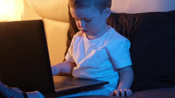 Leuke blonde blanke jongen alleen in de slaapkamer 's nachts zitten op bed, typen op laptop toetsenbord, surfen of trawlen internet. Nachtlampje in de kamer, maanlicht door het raam. Dolly glijdt door video. — Stockvideo