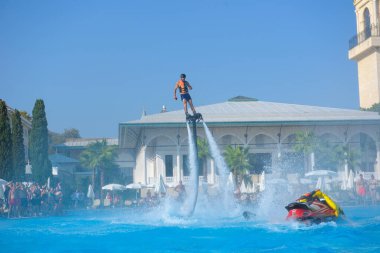 ANTALYA TURKEY 27 SEPT 2019: uçan giysili adam havuz otelinde havuz jeti veya su basıncı kuvvetiyle uçuyor. Güneşli havada kaydediliyor, genel plan.