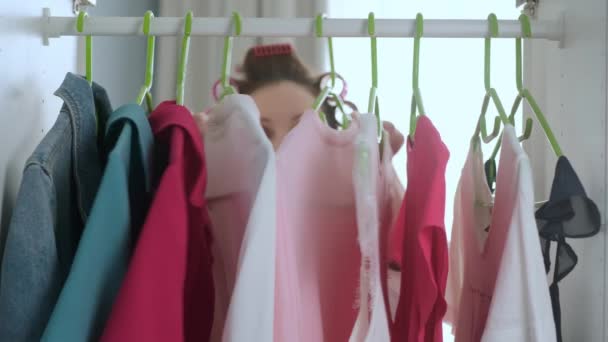 São Petersburgo, Rússia 20 de abril de 2020: Jovem em Roupão e rolos abre guarda-roupa na sala de estar e escolhe t-shirt branca, vestidos de mulher para andar, fecha guarda-roupa. Câmera dentro do armário — Vídeo de Stock