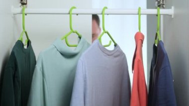 Tıraşsız, beyaz bir adam sabah gardırobu açar ve askıya gömlek asar, gardıroba gider, mavi tişört seçer, dolap kapılarını kapatır. Kamera görüntüsü Gardıropta