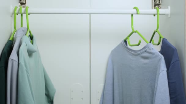 L'homme caucasien ouvre sa garde-robe dans la chambre le matin et accroche un t-shirt couleur carotte sur un cintre, une garde-robe aux portes des placards. voir caméra à l'intérieur du casier. — Video