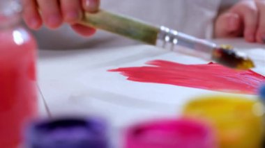 Küçük boyacı çocuk, beyaz kağıt ya da tuval üzerine sarı guaj boyalı fırçayla farklı renklerde kırmızı ve sarı boya paletini karıştırarak resim çizer. Sanatçı resim çiziyor.