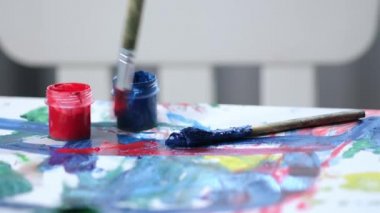 Ressam resim çizer, ressam fırçayı kırmızı boya kavanozuna koyar ve resim tuvaline soyut kırmızı fırça darbeleri çizer. Sanat ve çizim kavramı