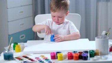 Parlak beyaz tişörtlü, sarışın beyaz çocuk ellerini mavi el boyasıyla boyamış ve tuvale el izi koymuş, çocuklar ellerini kâğıda çizerek sanatsal sanatla meşgul olmuş..
