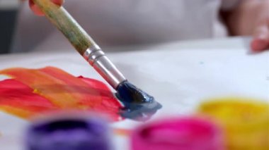 Küçük sanatçı çocuk beyaz kağıda mavi gouache boya ile fırça ya da resimli tuval ile resim çizer, farklı arkaplan renklerine palet çizer. Ressam resimlerin sanatsal çizimleriyle ilgilenir.