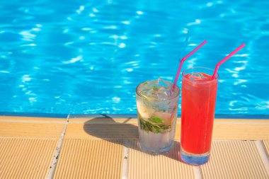 İki ferahlatıcı kokteyl Mojito ve Cosmopolitan yaz sıcağında arka planda bulanık bir şekilde havuzun kenarında duruyorlar. Dinlenme ve seyahat konsepti pahalı bir tatildir. metin için yer.