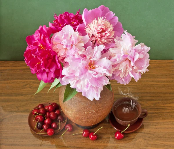 Still life with huge bunch red and pink peonies, red cherries and tea cup on painting background — Stock Photo, Image