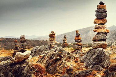 Taştan yapılmış küçük renkli piramitler ve arkasında da dağ silindirleri var.