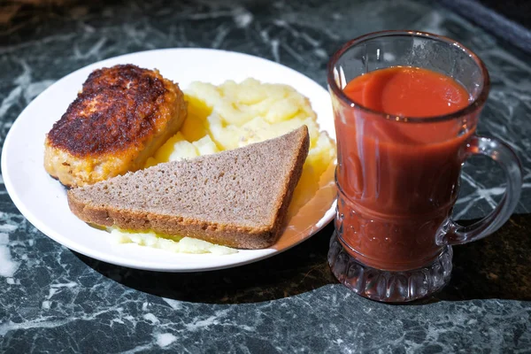 Cutlet and mashed potatoes and bread on a plate and a glass of tomato juice — Stock Photo, Image