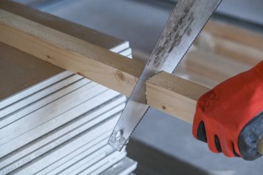 İşçi demir testeresiyle tahta bir bloğu kesiyor.