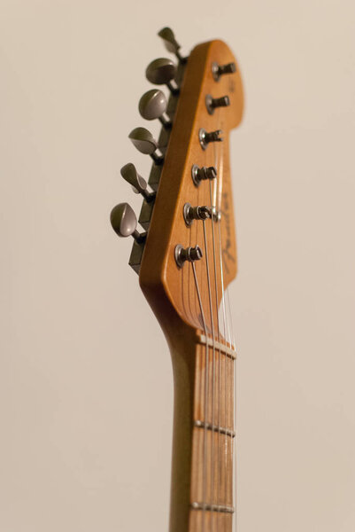 Vintage worn electric guitar head and neck close up with retro tuners, isolated on beige background