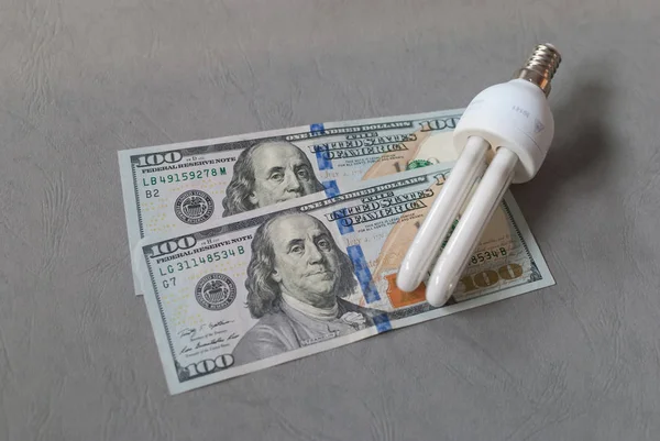 Energy saver light bulb  laying on two 100 dollar bills