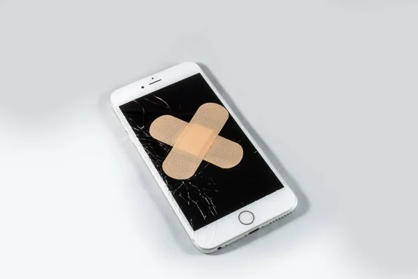 White iPhone with broken screen with plastic band aid — Stock Photo, Image