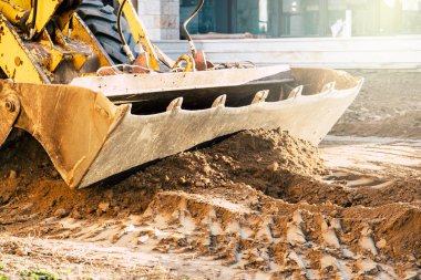 Kazıcı inşaat alanında kürekle toprağı hareket ettiriyor.