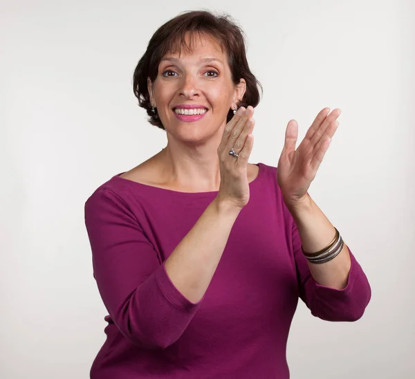 Vrouw in paars shirt op een witte achtergrond klappen. — Stockfoto