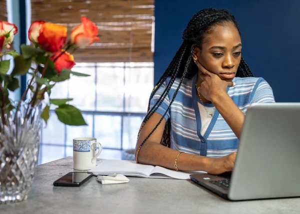 Genç, Afro-Amerikalı bir kadın laptopuyla evden çalışıyor.