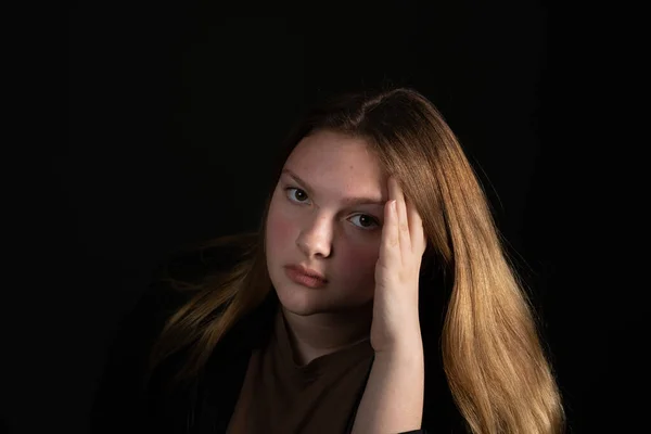 Sad teen girl on a black background with head in hands. Teen Depression concept.
