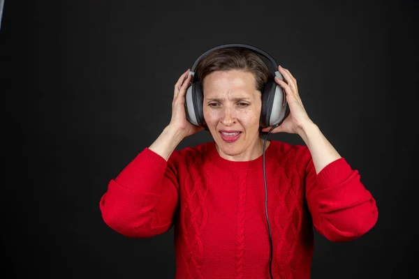 Oudere vrouw met een set van retro bekabelde koptelefoon in een rode trui dansen en genieten van muziek. — Stockfoto