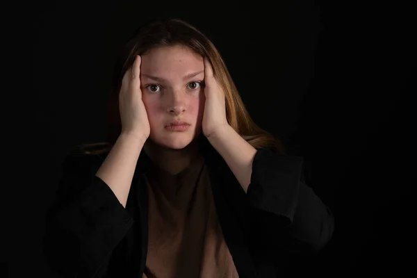 Sad teen girl on a black background with head in hands. — Stock Photo, Image