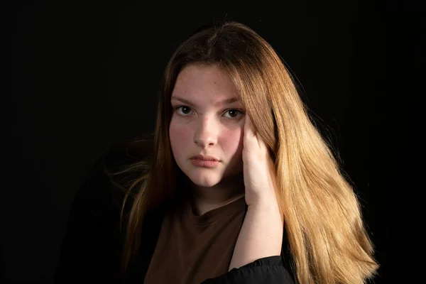 Triste menina adolescente em um fundo preto com a cabeça nas mãos . — Fotografia de Stock