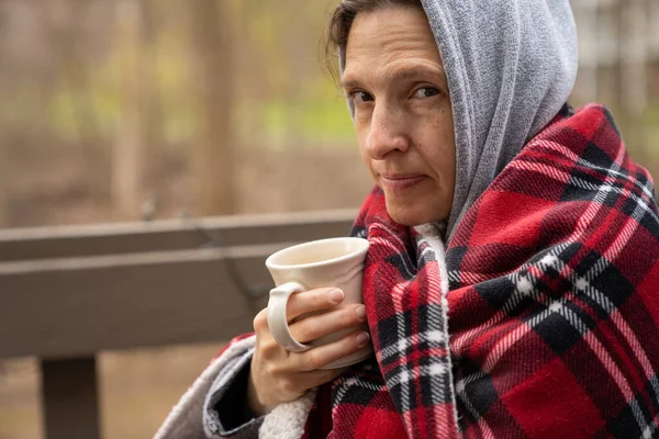 Middelbare leeftijd vrouw verpakt in een geruite wollen deken met koffie. — Stockfoto