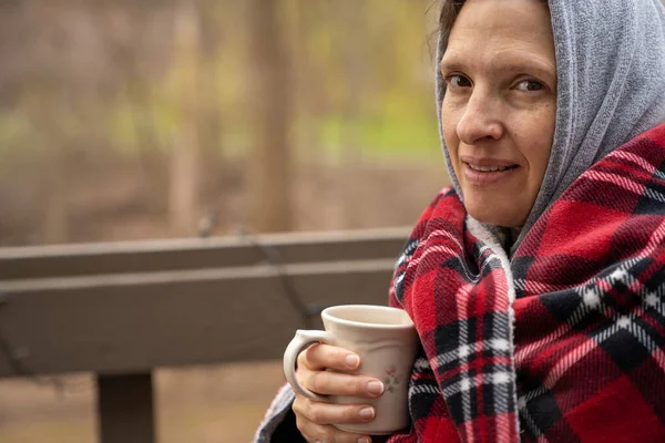 Donna di mezza età avvolta in una coperta di lana plaid con caffè . — Foto Stock