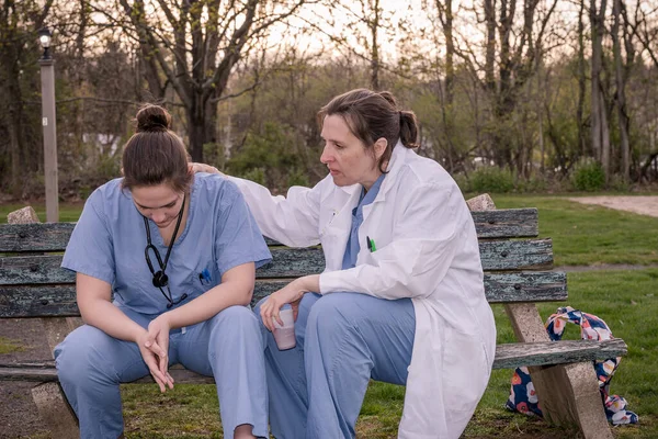 Önlüklü iki üzgün hemşire bir bahar akşamı dışarıda mola veriyor. Aşırı çalışan sağlık çalışanları konsepti.