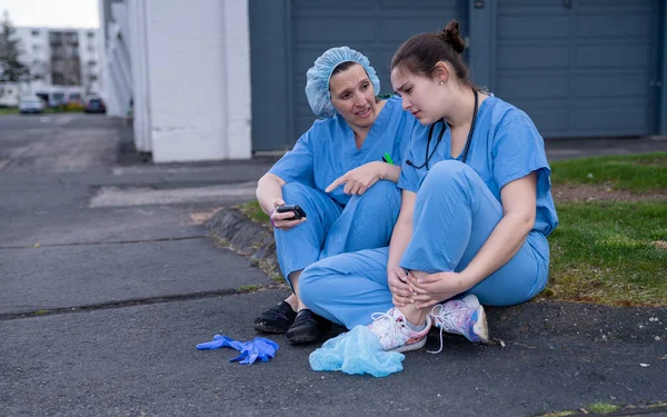 Önlüklü iki üzgün hemşire bir bahar akşamı dışarıda mola veriyor. Aşırı çalışan sağlık çalışanları konsepti.
