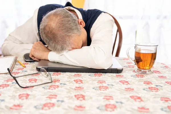 Man van middelbare leeftijd met een bril die thuis in de eetkamer werkt op een heldere dag in slaap. — Stockfoto