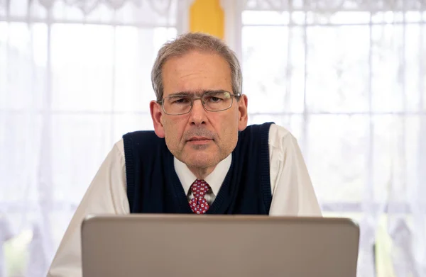 Gözlüklü orta yaşlı bir adam aydınlık bir günde yemek odasında laptopa bakıyor. — Stok fotoğraf