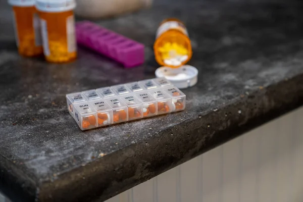 Multiple types of Prescription pills coming out of bottle, with daily container on counter top