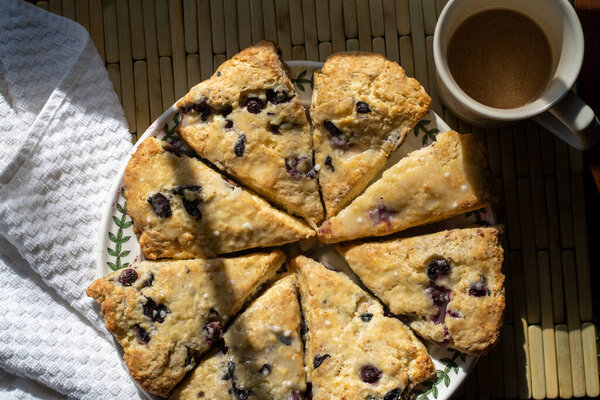 Черничные булочки, вырезанные треугольниками на круглой тарелке с чашкой горячего напитка
. 