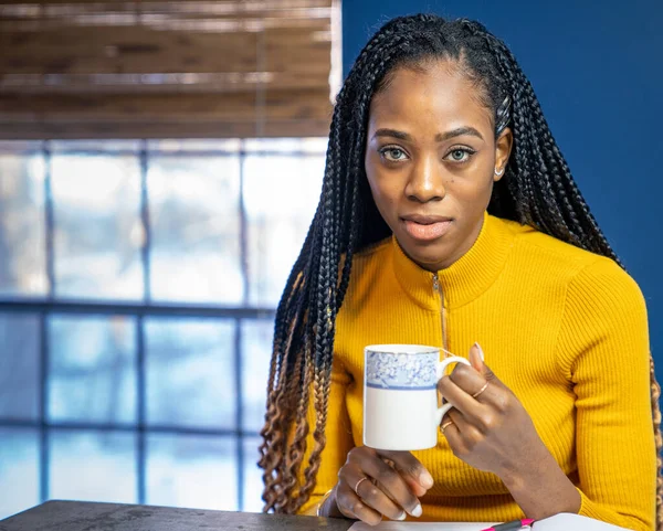 Young African American woman with yellow shirt sitting at the kitchen counter island doing homework. — Stock Photo, Image