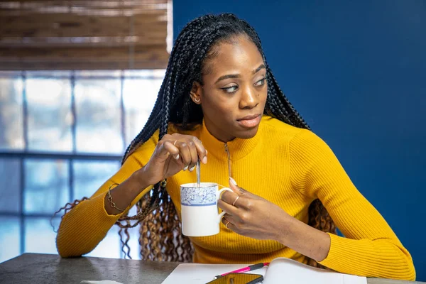 Young African American woman with yellow shirt sitting at the kitchen counter island doing homework. — Stock Photo, Image