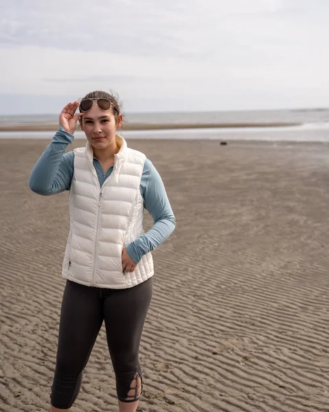 Caucasian young woman walking on beach looking into camera with sunglasses lifted. — Stock Photo, Image