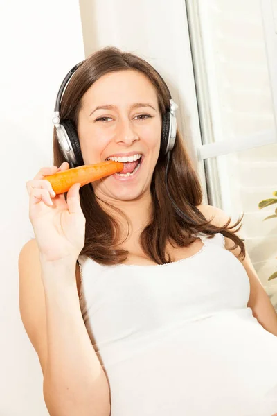 Feliz Joven Embarazada Comiendo Zanahoria Escuchando Música Través Auriculares — Foto de Stock