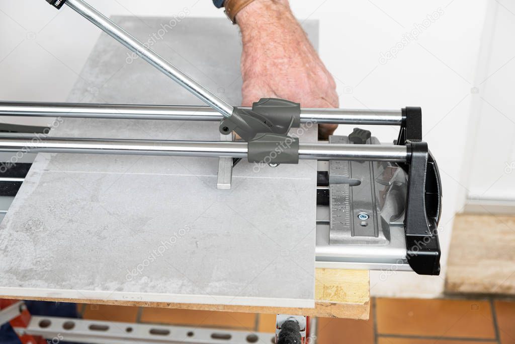 the mason cuts a ceramic tile with a tile cutter