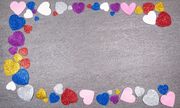 Corazones coloridos de brillo de todos los colores en un respaldo de granito gris — Foto de Stock