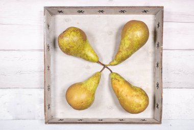 Dört konferans armudu eski ahşap bir zeminde eski bir ahşap tepsiye yerleştirilmiş.