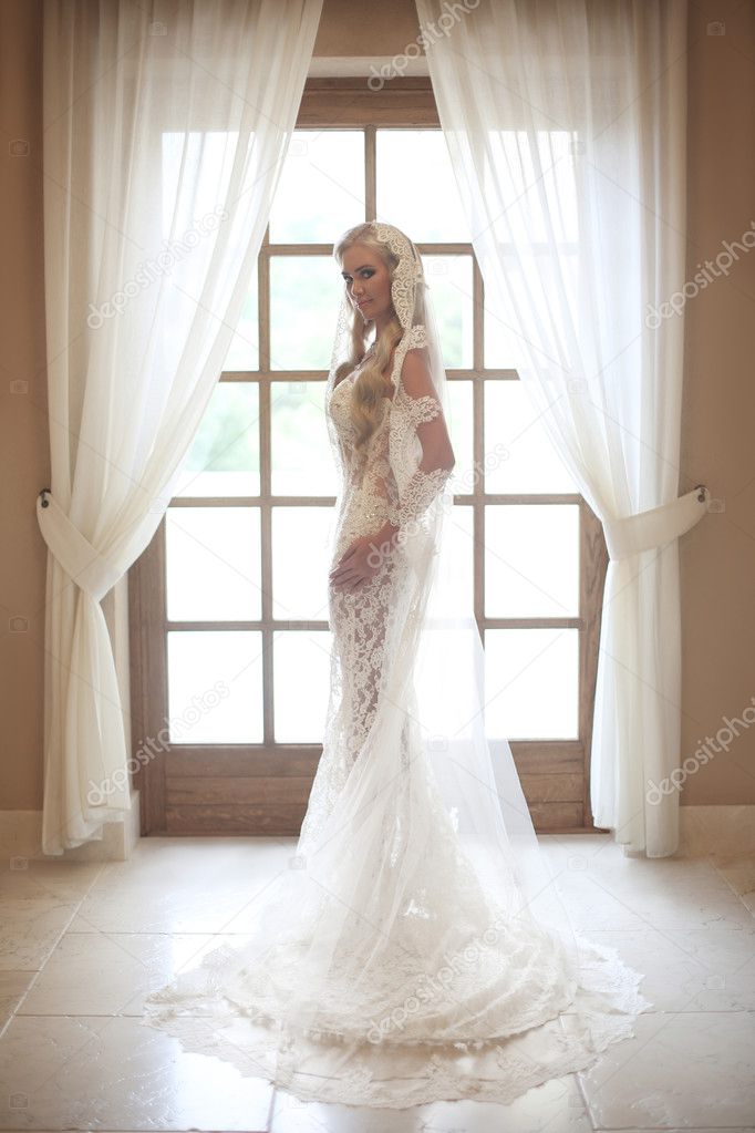 Beautiful bride in wedding dress with long bridal veil posing by