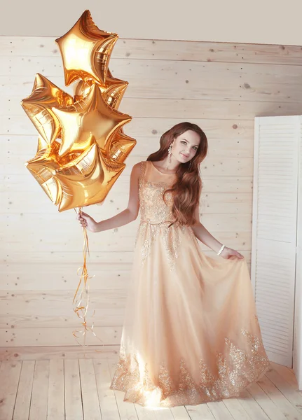 Junge hübsche Frau mit goldenen Sternballons über hölzernem beige b — Stockfoto