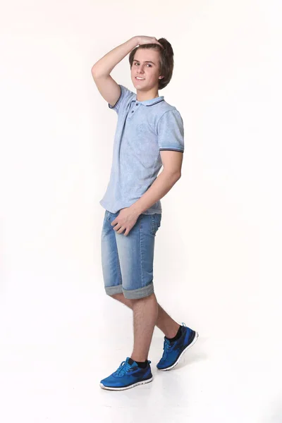 Молодой человек моды позирует в джинсовых шортах и синих кроссовках — стоковое фото