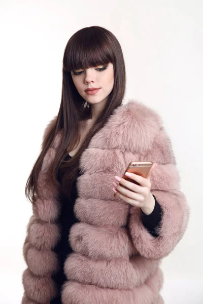 Fashionable brunette girl in pink fur coat holding mobile phone — Stock Photo, Image