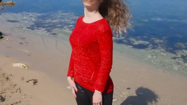 Крупним планом портрет жінки, що біжить рукою через кучеряве волосся, що дме у вітрі морем на пляжі. Щаслива жінка над блакитним небом . — стокове відео